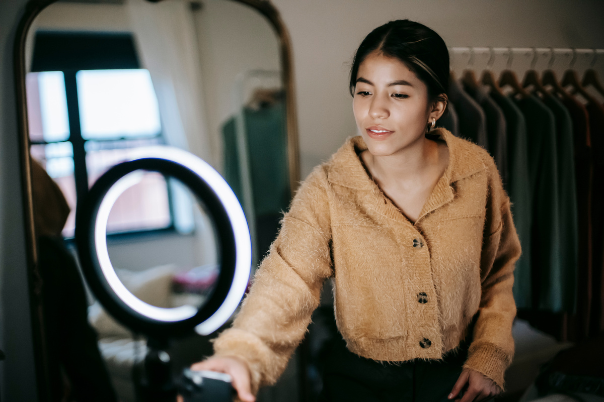 Ethnic female blogger filming video on cellphone with light lamp